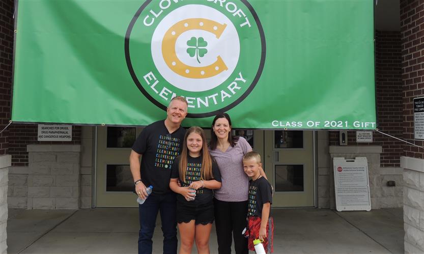 A family poses underneath a Clovercroft Elementary flag